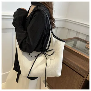 Detail of cream tote bag featuring black contrast trim and a delicate ribbon bow