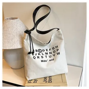 Dettaglio della borsa tote in tela crema con stampa alfabeto nero e tracolla annodata