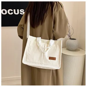 Detail of white corduroy tote bag featuring dual front pockets and brown leather brand label