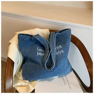 Detail view of denim tote bag with Less Mondays More Holidays embroidery on vintage chair