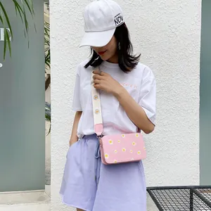 Pink crossbody square bag featuring white daisy prints and a wide canvas shoulder strap