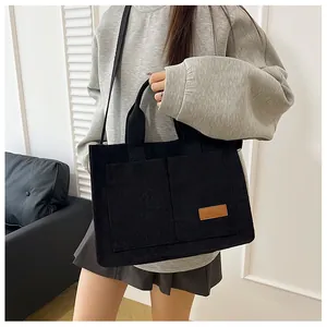 Detail view of black corduroy tote bag showing fashion label and textured fabric surface