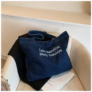 Detailed close-up of dark blue denim tote bag featuring white Less Mondays More Sundays embroidery