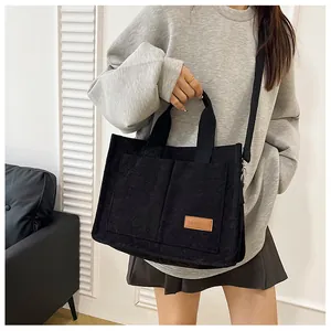 Close-up of black corduroy tote bag featuring a leather fashion label and adjustable strap