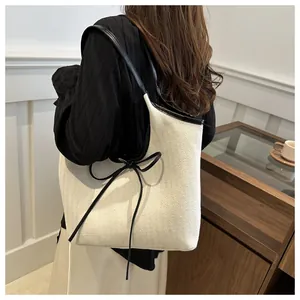 Detail of canvas tote bag with black leather straps and decorative bow accents