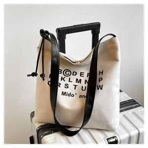 Dettaglio della borsa tote in tela crema con stampa di lettere nere e tracolla in pelle