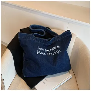 Close-up of dark blue denim tote bag with Less Mondays More Sundays white embroidery