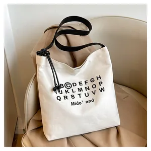 Dettaglio della borsa tote in tela beige con stampa alfabeto e tracolla in pelle
