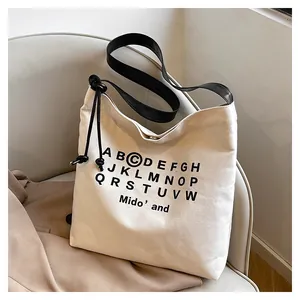 Dettaglio della borsa tote in tela color crema con stampa alfabeto su sedia grigia