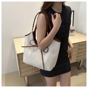 Detail of cream canvas tote bag with brown leather handles and decorative bow accent