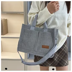 Detail of grey corduroy tote bag showing large front pockets and stylish leather label