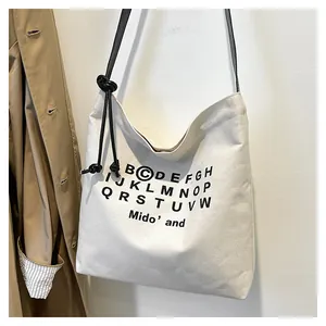 Dettaglio borsa tote in tela crema con stampa tipografica nera e manici in corda annodati