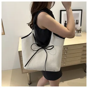 Detail of herringbone canvas tote bag with black leather bow accent on a female model