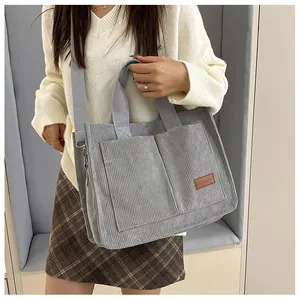Close-up of grey corduroy tote bag featuring dual front pockets and brown fashion leather patch