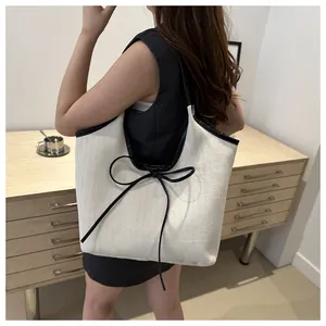 Detail of a beige herringbone tote bag with black leather straps and bow on shoulder