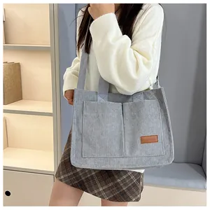 Detail of grey corduroy tote bag with large front pockets and brown leather brand label