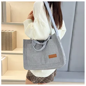 Macro view of light grey corduroy tote bag featuring a leather fashion label and front pocket