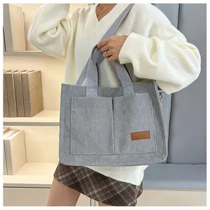 Detail of light gray corduroy tote bag showing large pockets and a brown leather fashion tag