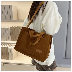 Detail of brown corduroy tote bag featuring adjustable strap and fashion label on front pocket
