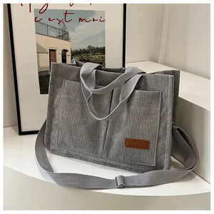 Detail of light gray corduroy tote bag showing large front pockets and long shoulder strap