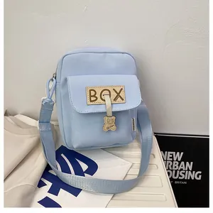 Detail of light blue canvas crossbody bag with a bear charm and BOX leather label