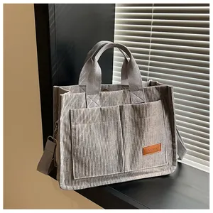 Detail view of corduroy tote bag featuring two front pockets and a leather FASHION label