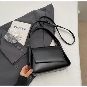 Detail van minimalistische zwarte PU handtas met klep en dubbele riemen op het bed geplaatst