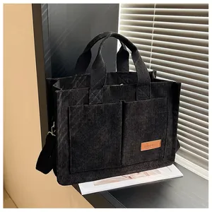 Detail of black corduroy tote bag showing textured fabric and front pocket fashion label