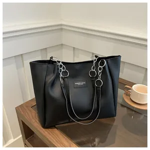 Detail of black tote bag with silver chain handles and fashion leather patch logo