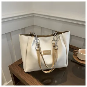 Detail of cream tote bag with brown handles and silver chain on a wooden table