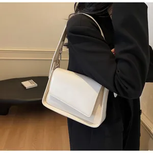 Detail van ivoren schoudertas met asymmetrische flap en brede riem op een zwarte blazer