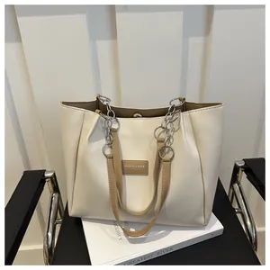 Detail of cream tote bag with brown handles and metal chain on a black chair