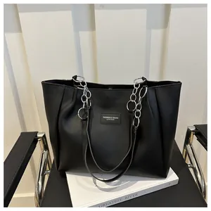 Detail view of black faux leather tote bag with silver chain strap and fashion label