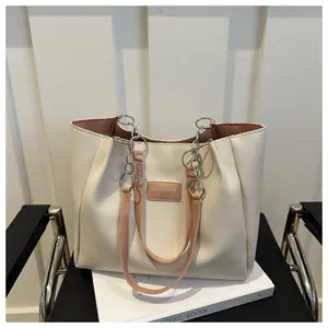 Close-up of leather tote bag with metal chain strap and logo tag detail on white chair