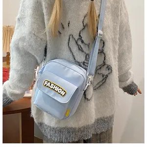 Light blue canvas crossbody bag with FASHION embroidery worn by model over a white sweater
