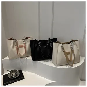 Three minimalist leather tote bags with metal chain straps and fashion labels