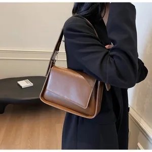 Close-up van een bruine leren schoudertas gestyled met een zwarte blazer voor een retro look