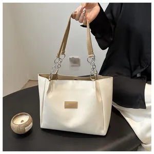Detail of cream tote bag with light brown handles and silver chain link decoration