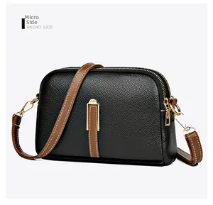 Detail of black lychee grain leather crossbody bag with brown contrast stitching and gold zippers