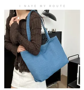 Detail of a large blue denim tote bag worn by a model in casual knitwear outfit