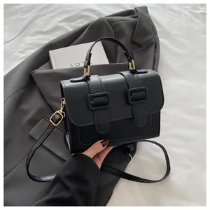 Detail of black crossbody square bag with gold buckles and adjustable strap