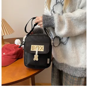 Detail of black canvas crossbody bag with BOX patch and cute cartoon bear pendant