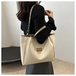 Detail of a large cream tote bag with brown leather tag and metal chain shoulder strap