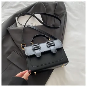 Detail of black leather square bag with gold metal studs and buckles on grey blazer