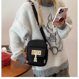 Close-up of black canvas crossbody bag with BOX patch and cute metal bear pendant