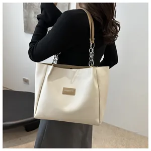 Detail of cream leather tote bag with metal chain strap and minimalist logo patch