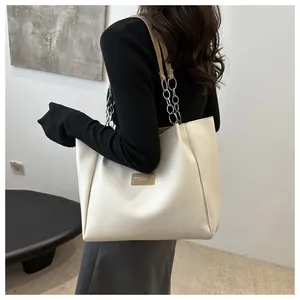 Detail of white leather tote bag featuring a metal chain strap and minimalist logo patch