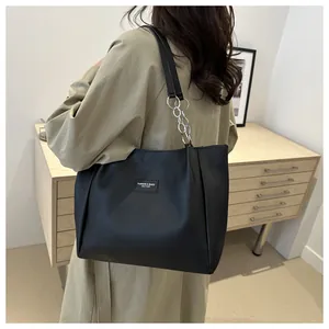 Detail of black leather tote bag featuring a metallic chain strap and fashion label