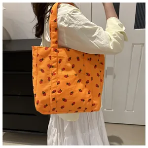 Detail van oranje corduroy draagtas met aardbeienprint gedragen door een model op de schouder