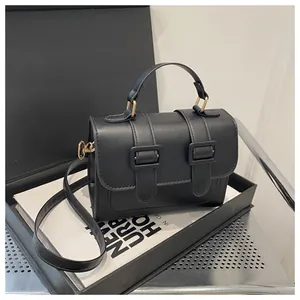 Detail view of black faux leather crossbody bag with twin buckle accents and curved handle